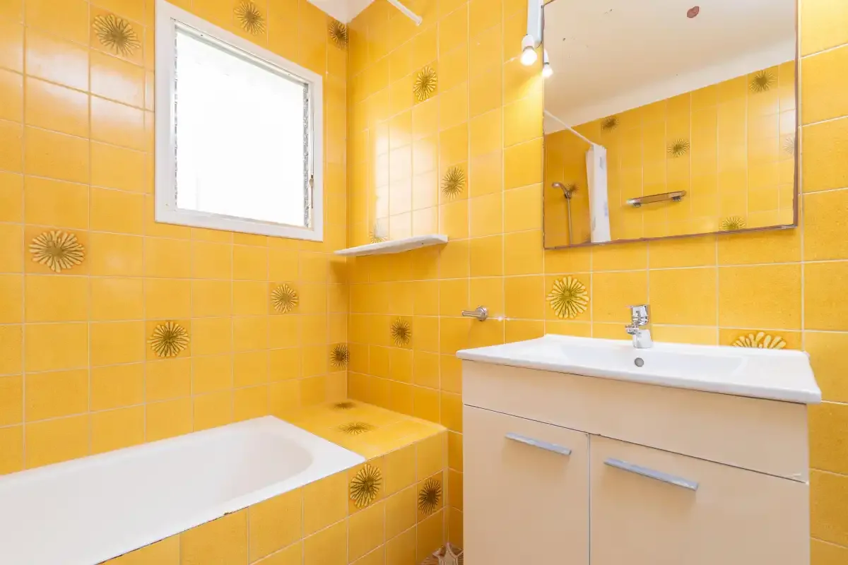 A bright bathroom with yellow tiled walls, a bathtub, and a vanity.