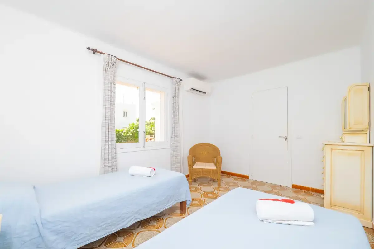A bright bedroom with two beds, a window, and a small wooden chair.