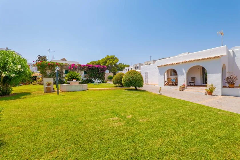 A landscaped garden with a broad lawn, flowering shrubs, and a white building.