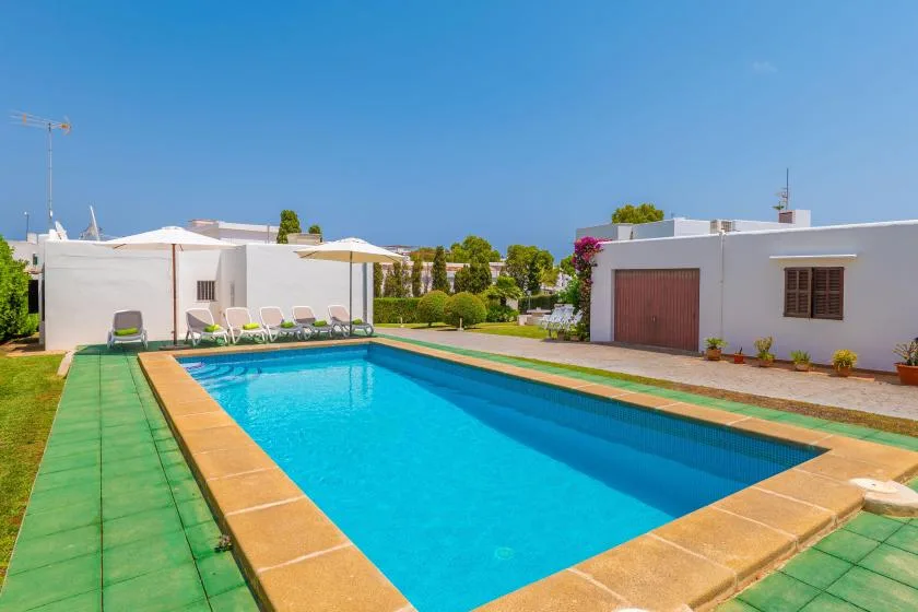 A rectangular swimming pool sits beside a white building and landscaped yard.