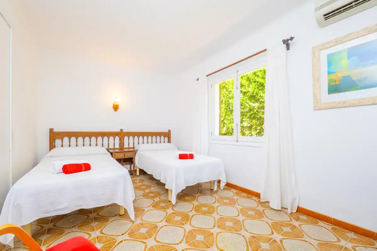 A bright bedroom with two beds and a window overlooking greenery.