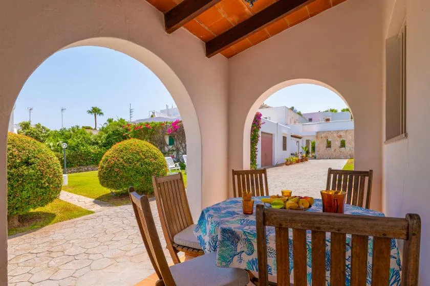 A covered outdoor dining area with a table overlooking a garden courtyard.