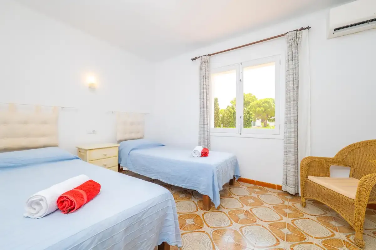 A bright bedroom with two beds and a window overlooking trees.