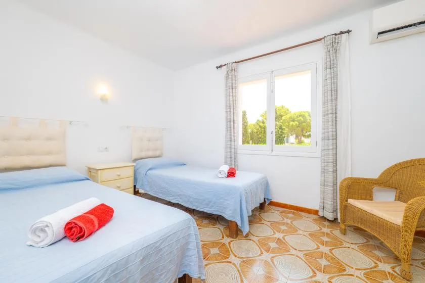 A bright bedroom with two beds, a window, and a wicker chair.