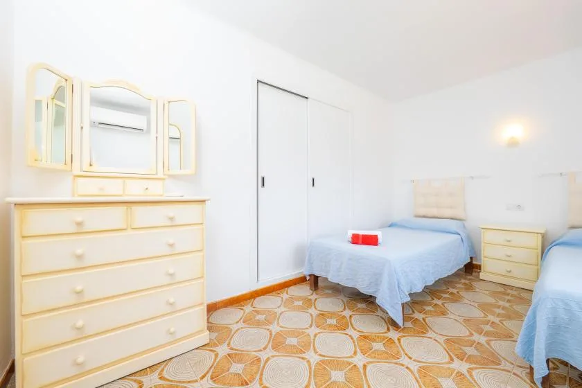 A bright bedroom with two beds, pale furnishings, and patterned tile flooring.