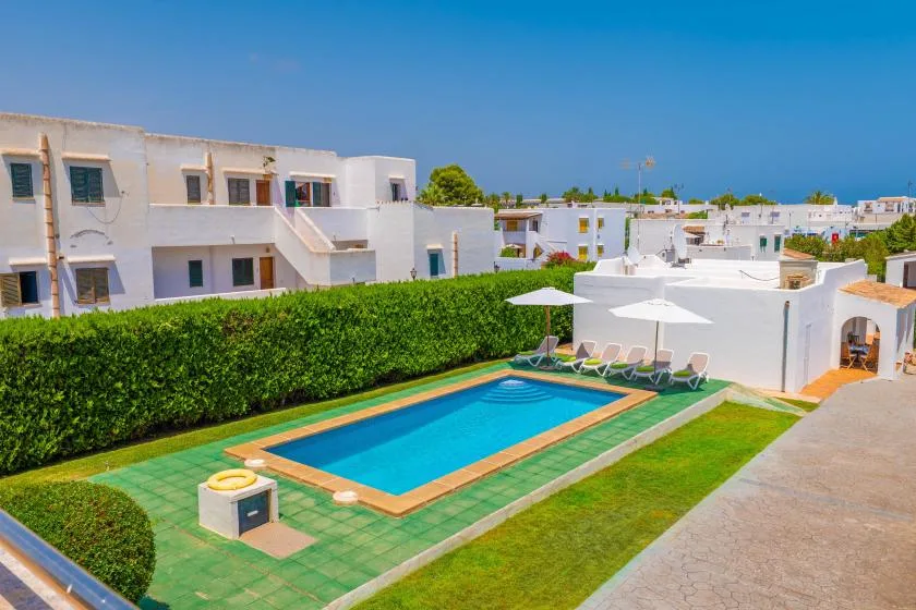 A rectangular swimming pool sits among white buildings and green landscaping.