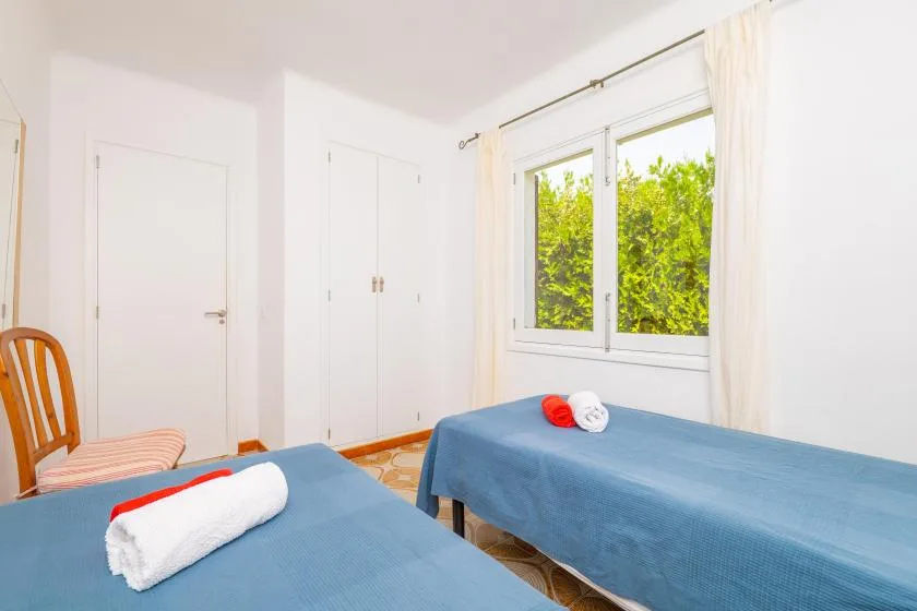 A bright bedroom with two beds covered in blue linens and a window overlooking greenery.