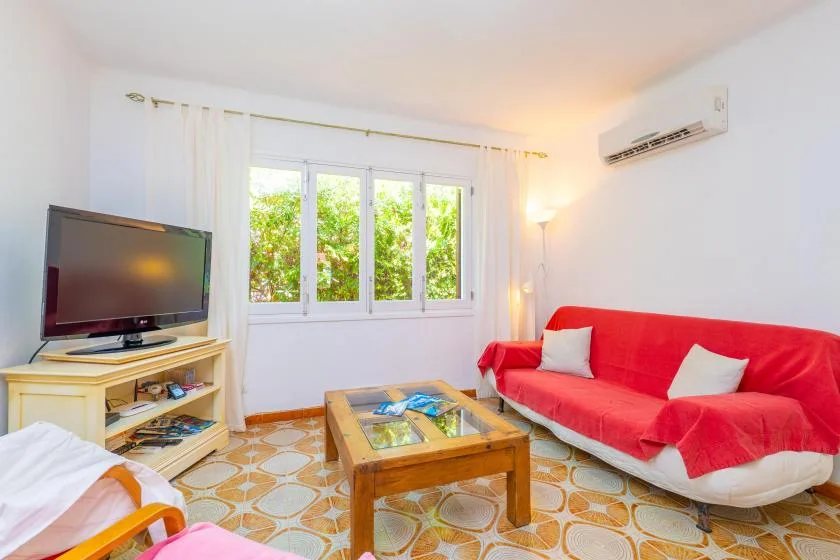 A living room with red seating, a television, and a coffee table by the window.