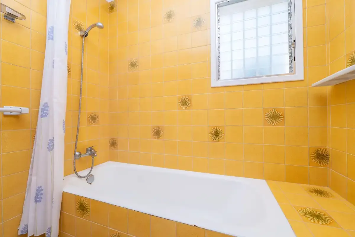 A bathroom with a bathtub, shower, and yellow tiled walls.