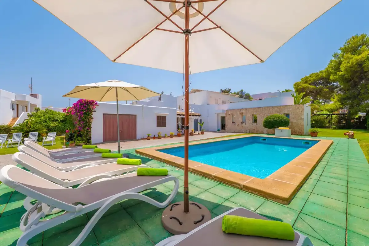 A sunny outdoor swimming pool is surrounded by lounge chairs and umbrellas.