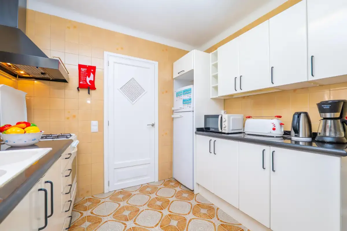 A bright kitchen with white cabinets, countertop appliances, and a patterned floor.