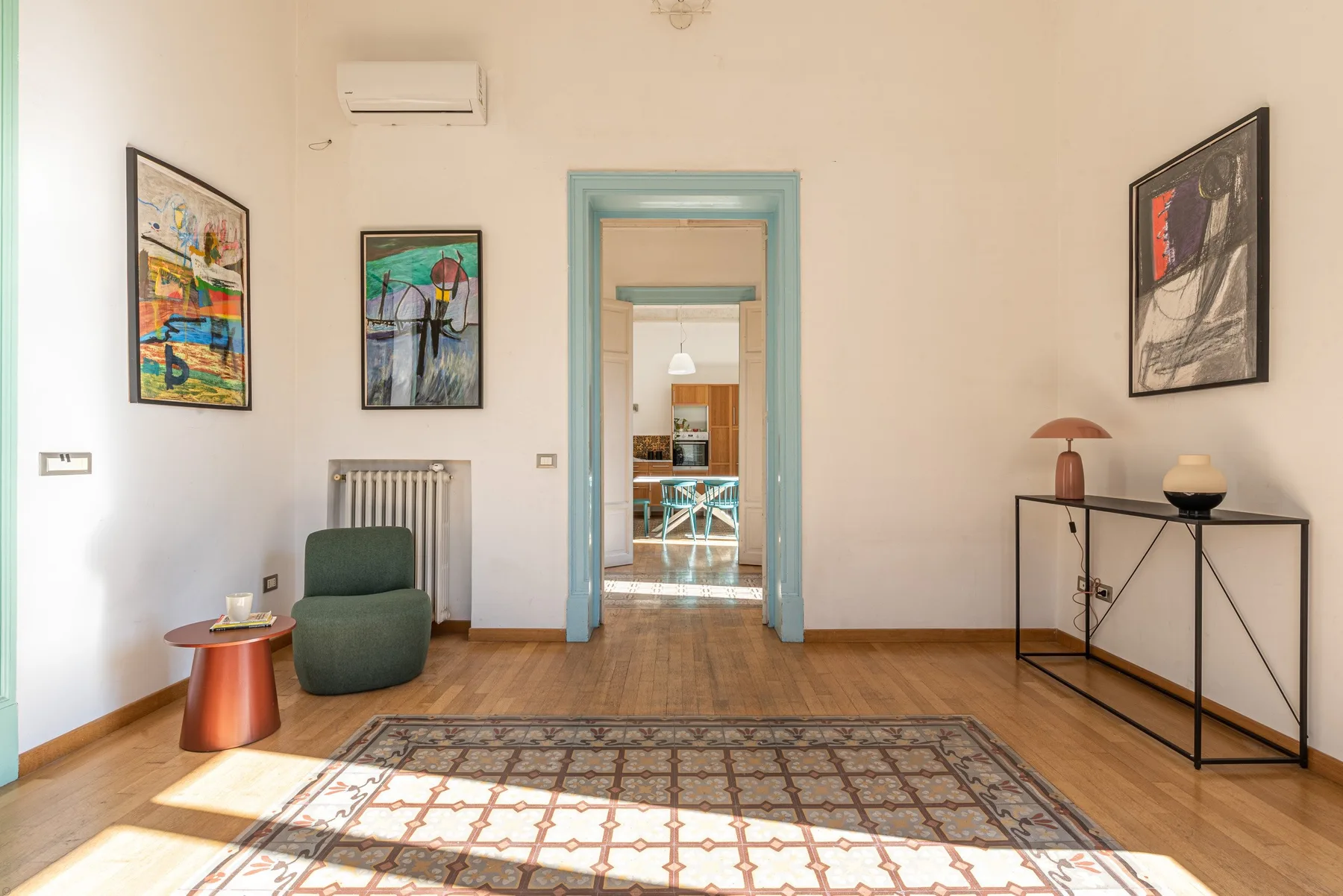 Una sala luminosa con una alfombra estampada y una puerta hacia el comedor.