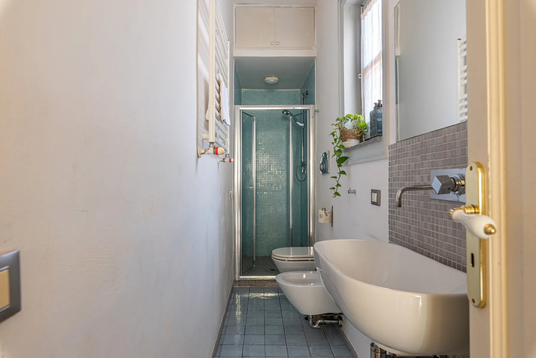 Un baño estrecho con bañera, lavabo y una ducha con mampara de vidrio.