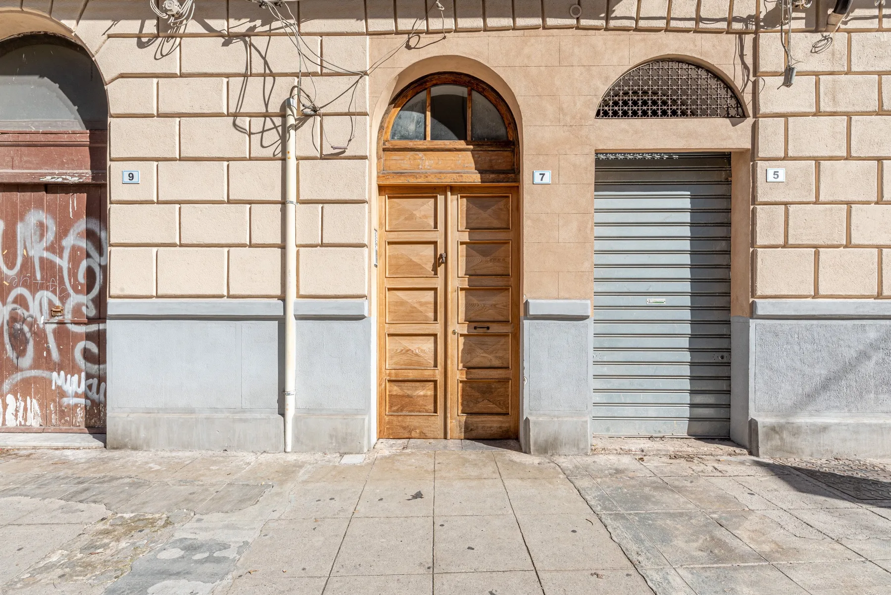 Fachada de un edificio a la calle, con una entrada de madera arqueada y una persiana metálica cerrada.