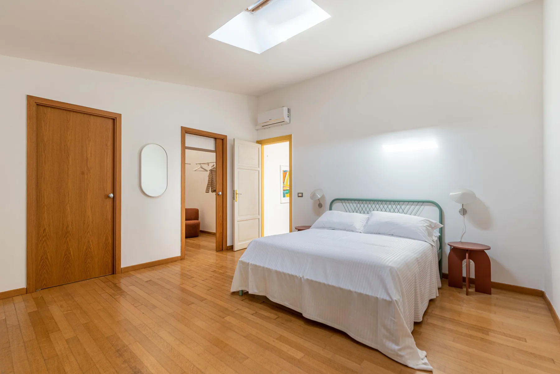 Un dormitorio con una cama bien arreglada, suelo de madera y una puerta abierta.