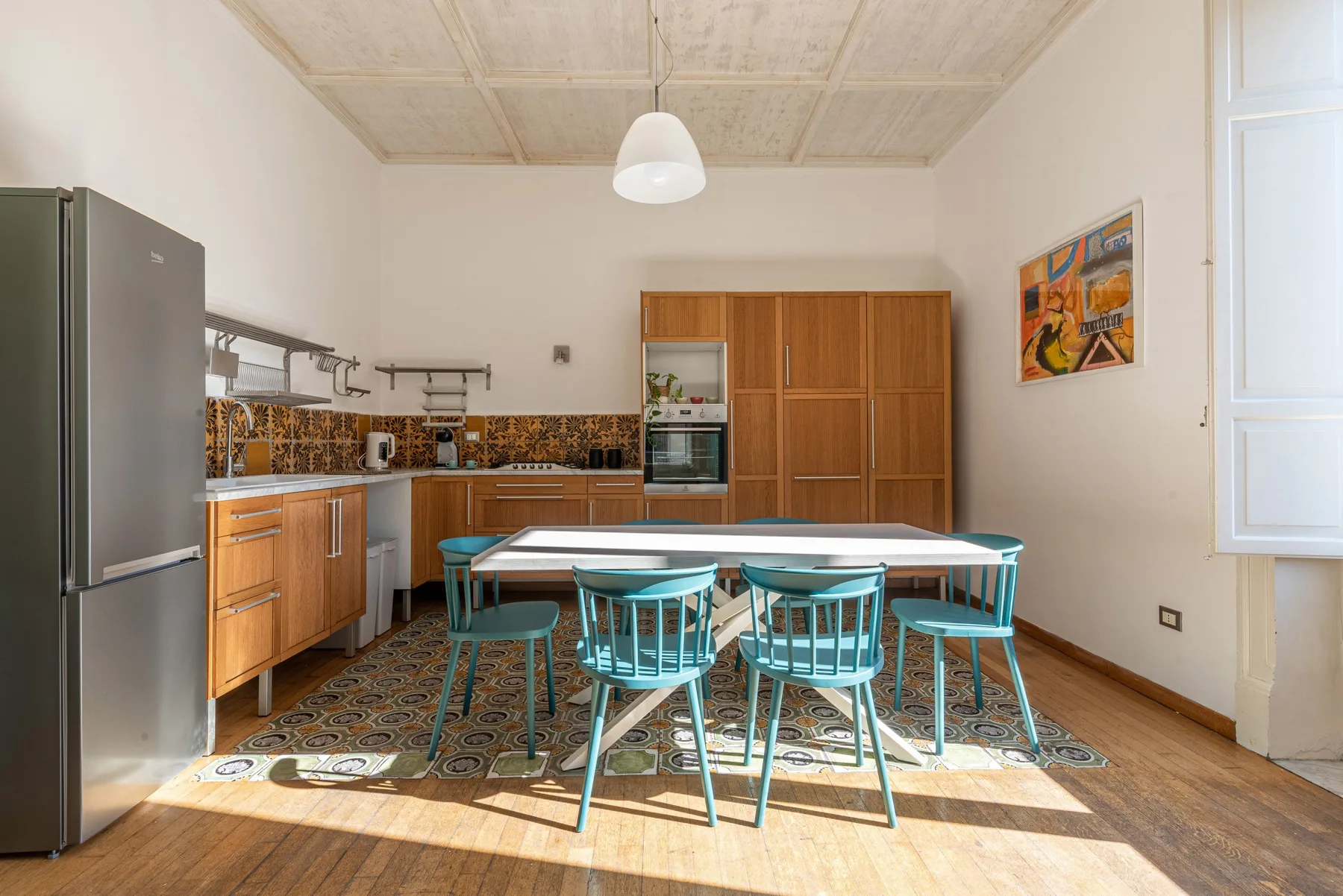 Una zona de comedor en la cocina con una mesa de madera y asientos turquesa.