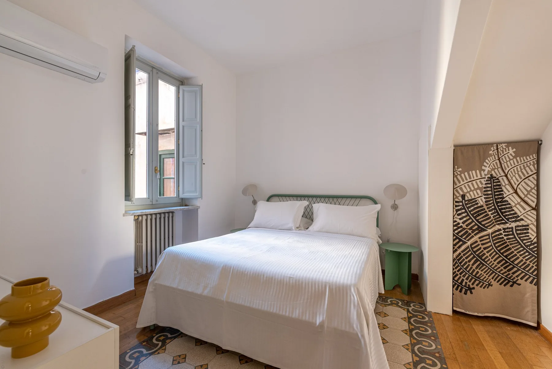 Un dormitorio luminoso con una cama doble junto a una ventana abierta.
