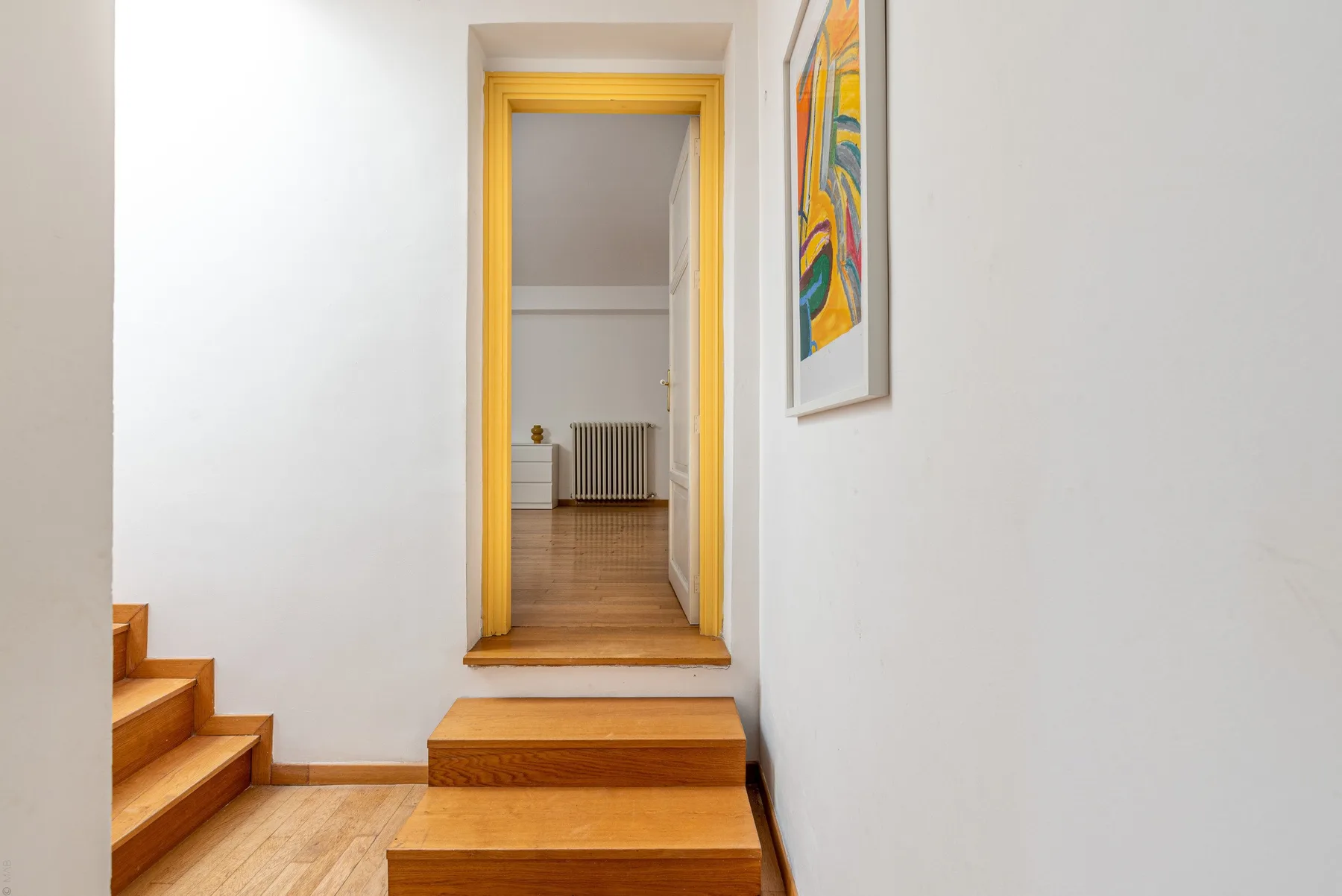 Una escalera de madera conduce por una puerta con marco amarillo a una habitación luminosa.