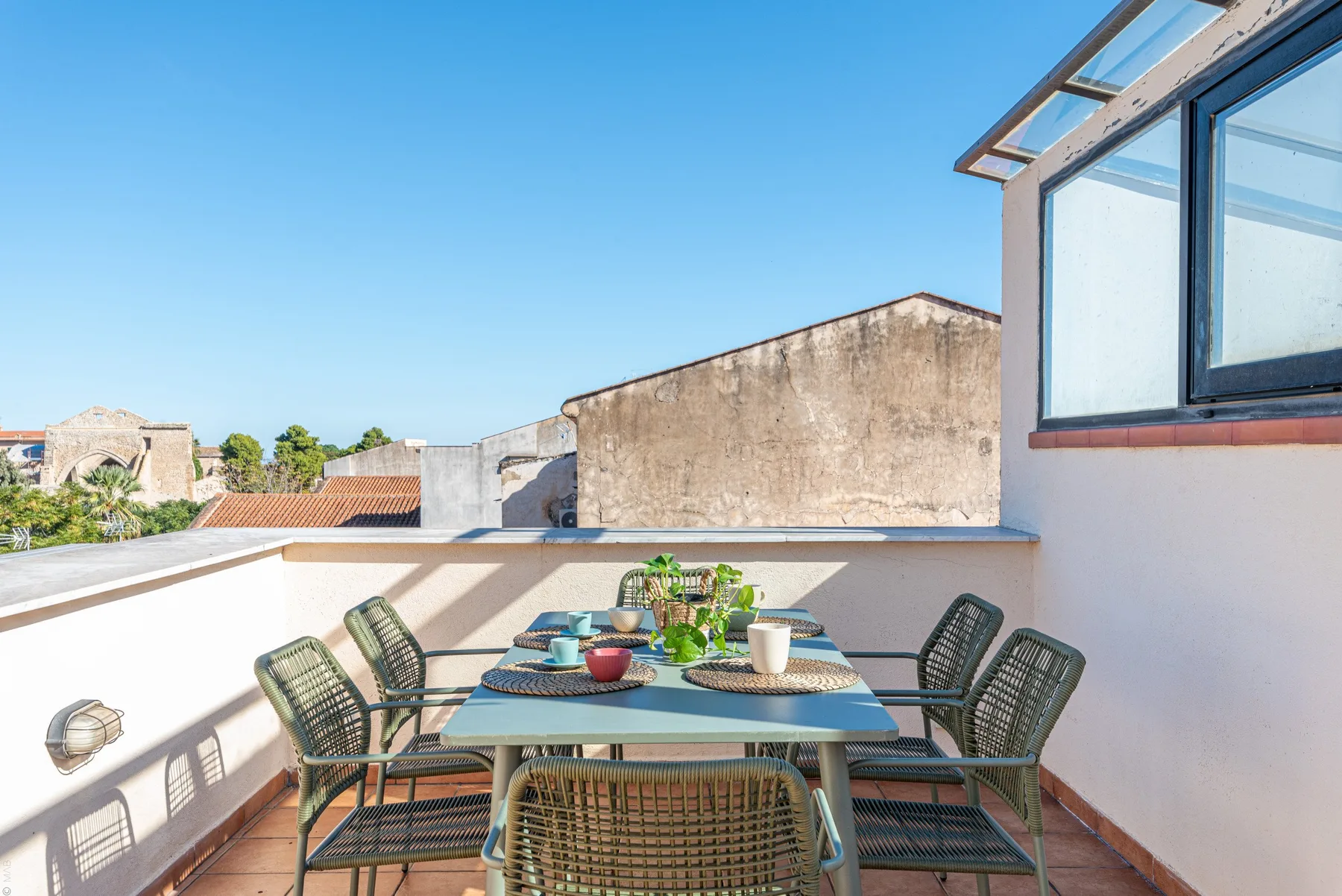 Comedor al aire libre en una terraza soleada, con una mesa y asientos.
