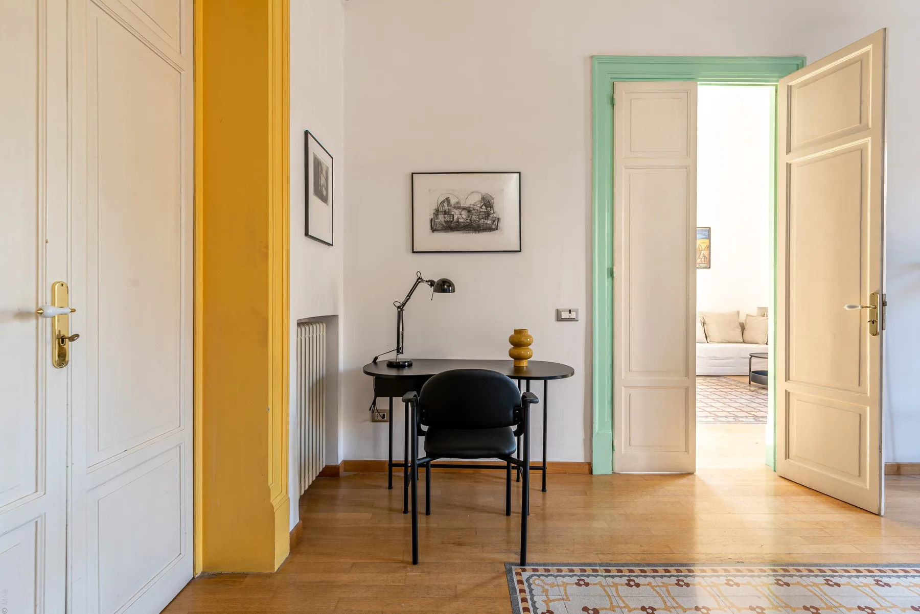 Un escritorio pequeño y una silla están en una habitación luminosa con puertas abiertas.