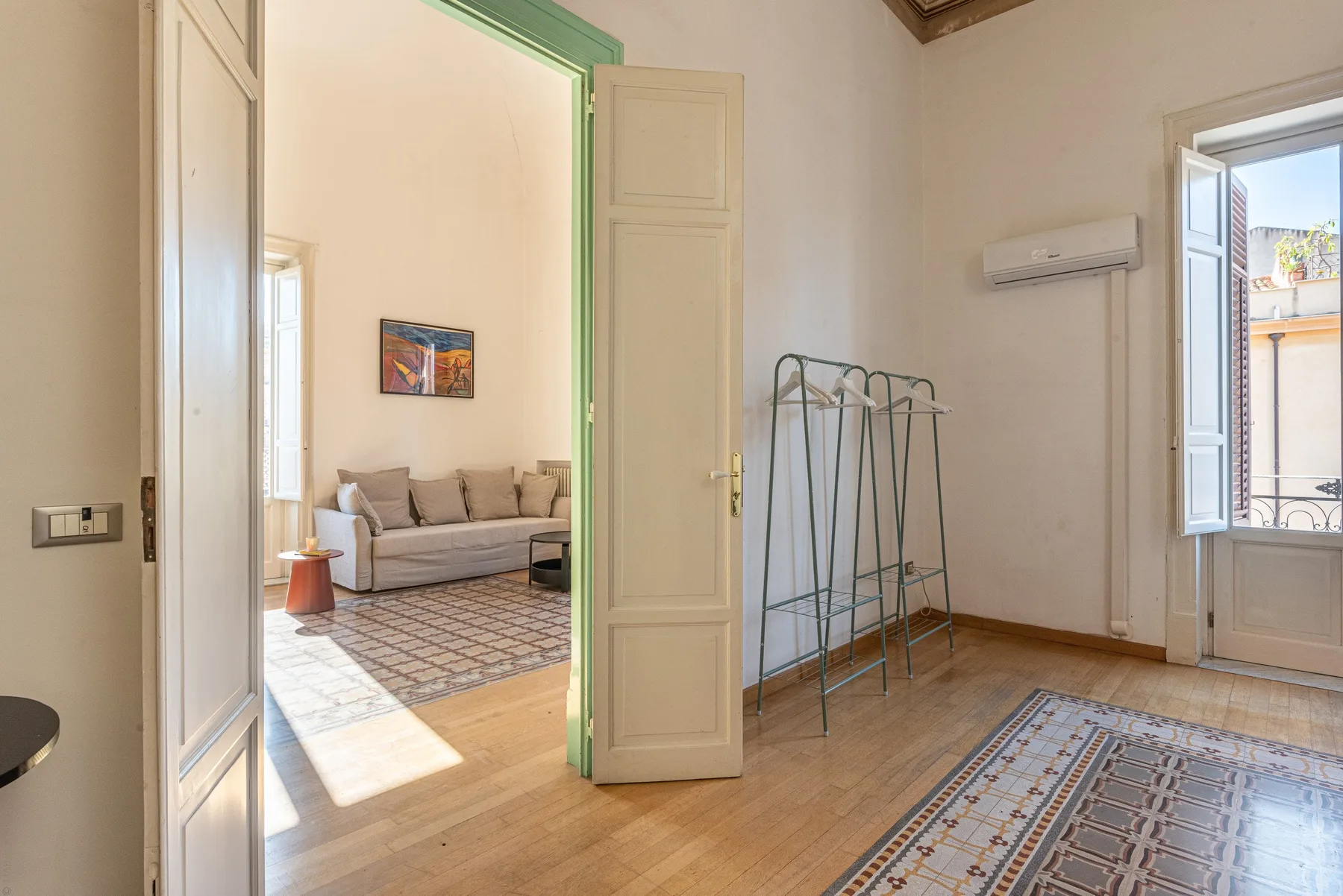 Una habitación luminosa con una puerta abierta hacia una zona de estar y una alfombra estampada.
