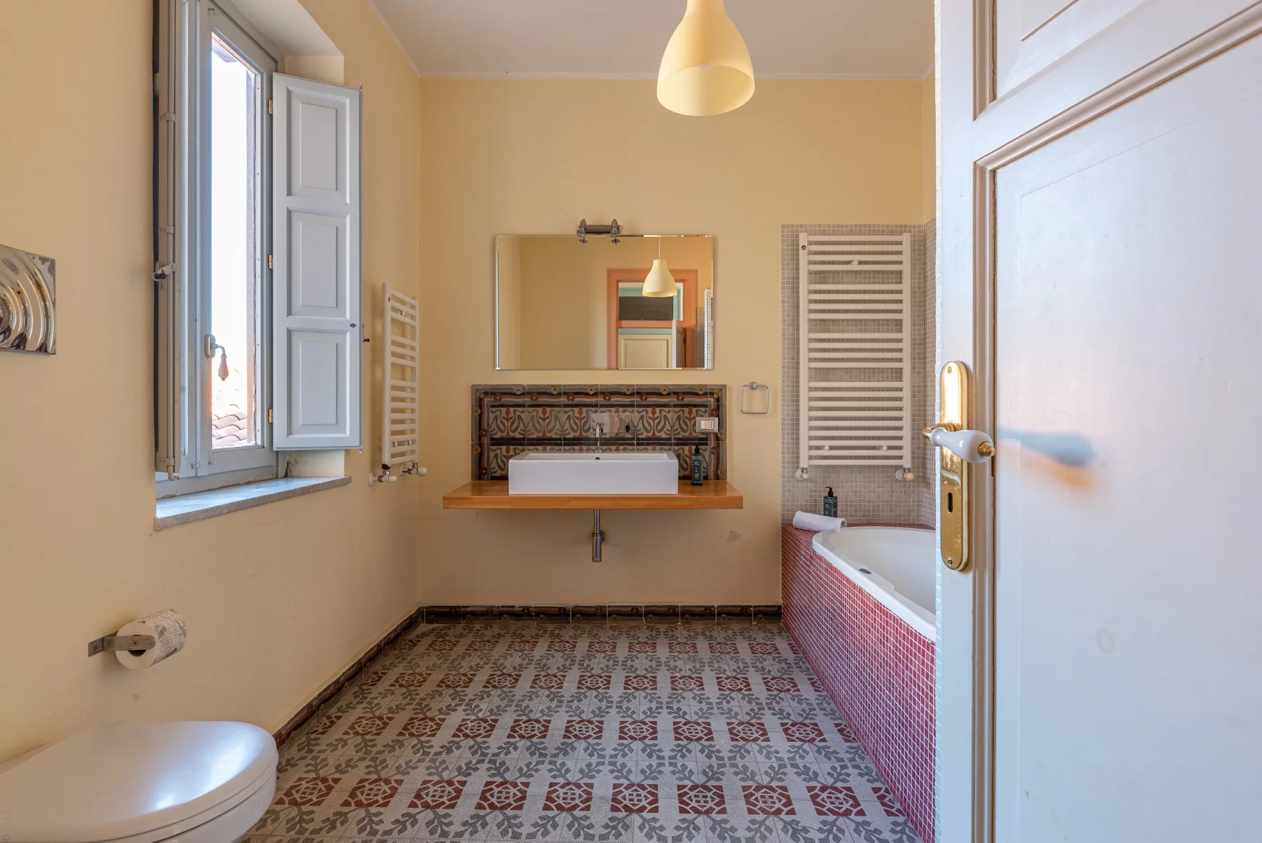 Un baño con suelo de baldosas estampadas, bañera y lavabo bajo un espejo.