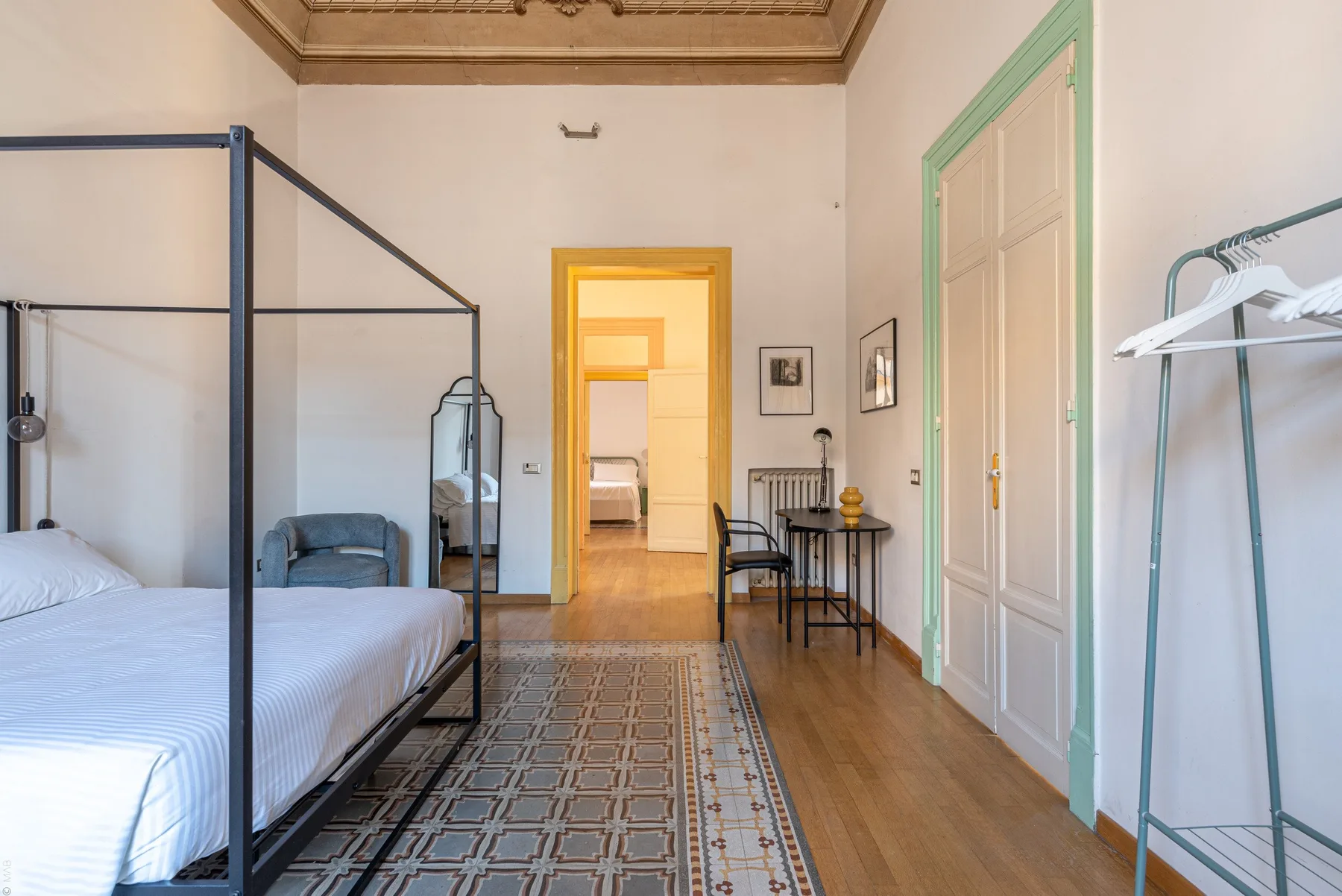 Un dormitorio con cama con dosel, alfombra estampada y una mesita junto a la puerta.