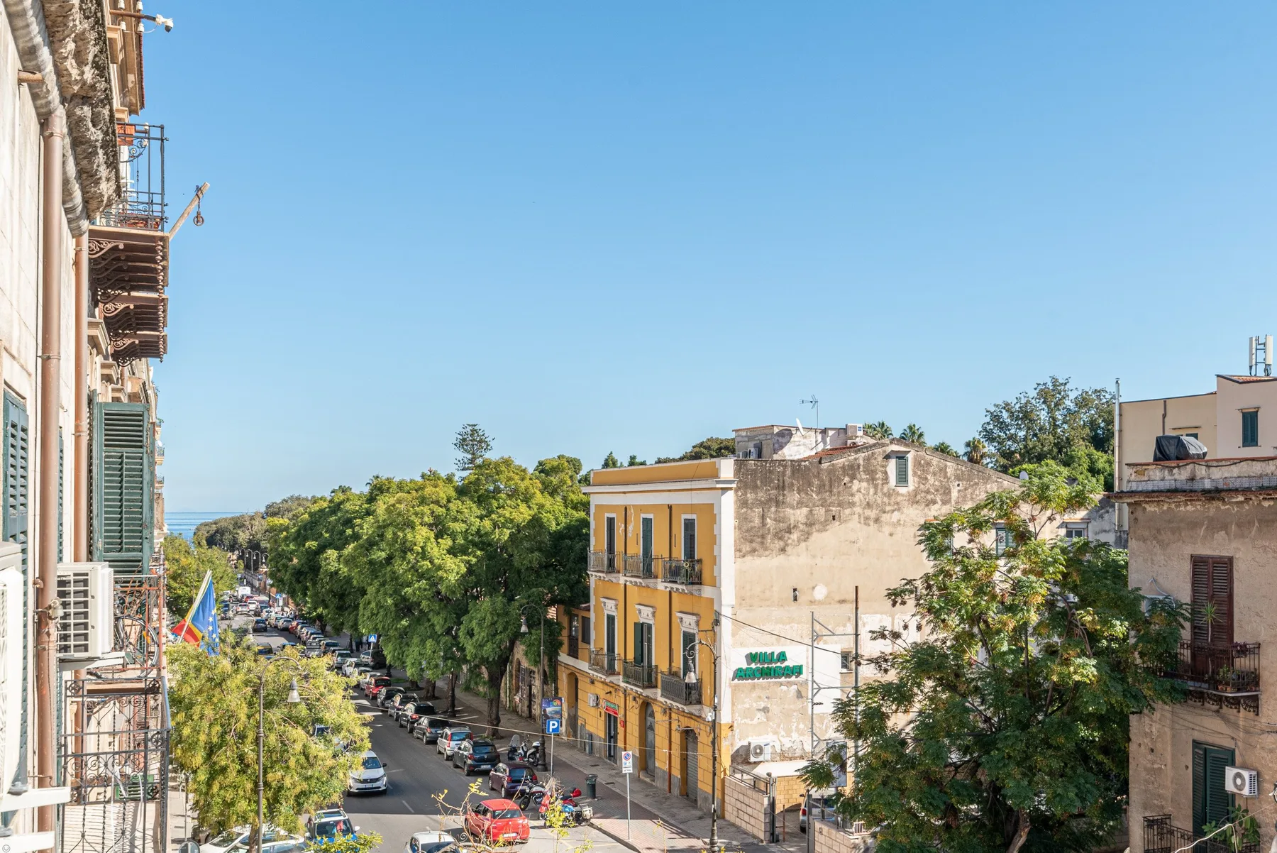 Una calle urbana bordeada de edificios y árboles frondosos bajo un cielo azul despejado.
