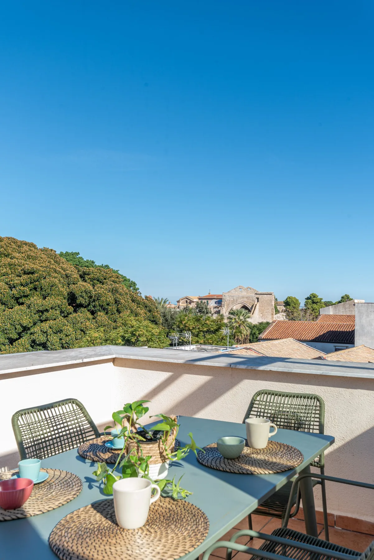 Una terraza soleada en la azotea con mesa, asientos y plantas en macetas.