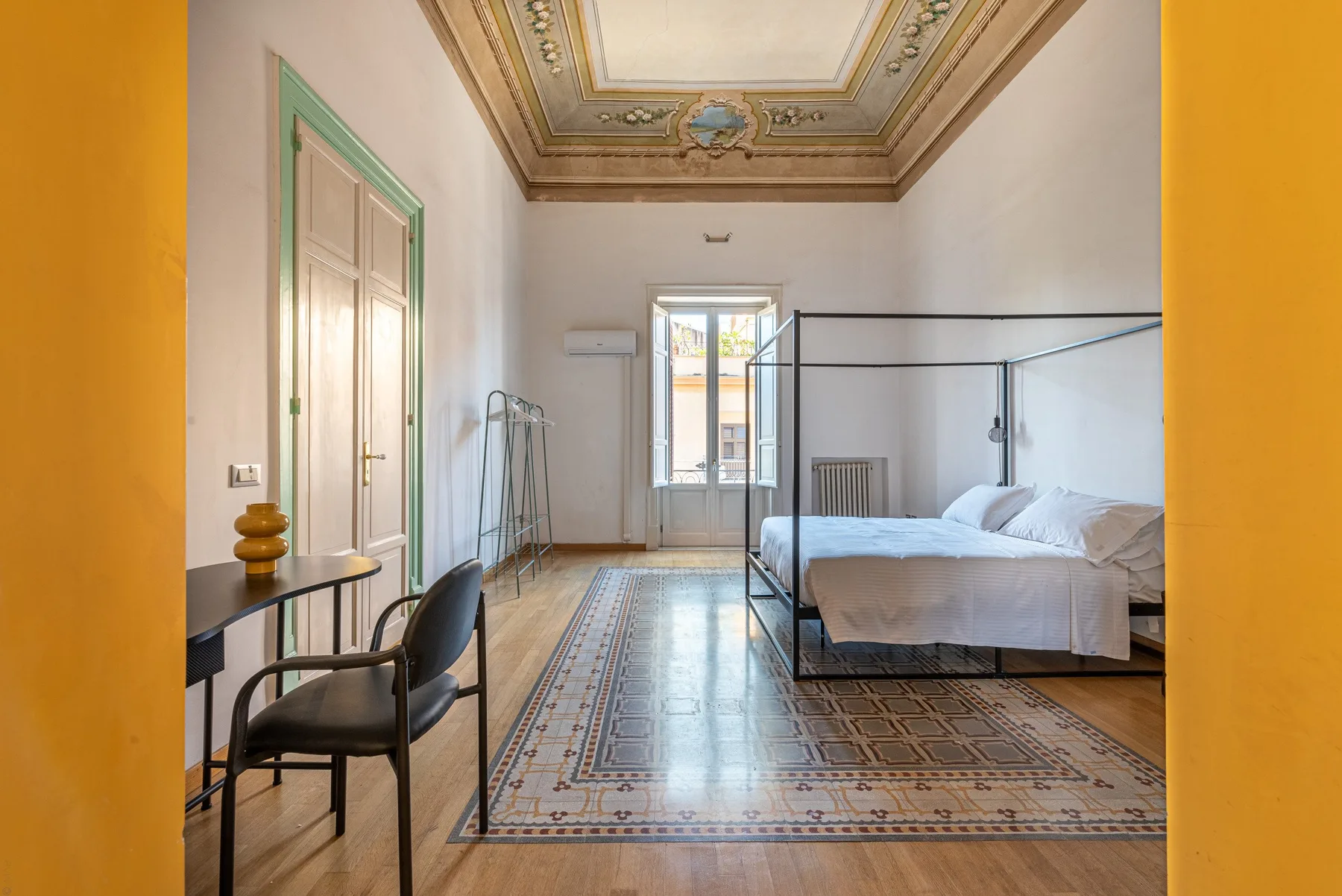 Un dormitorio luminoso con una cama grande, ventanas altas y un techo ornamentado.