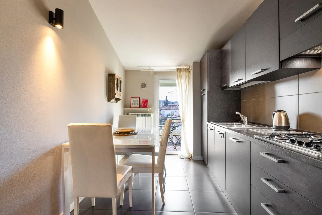 Una cocina compacta y zona de comedor con armarios oscuros y una mesa junto a la ventana.