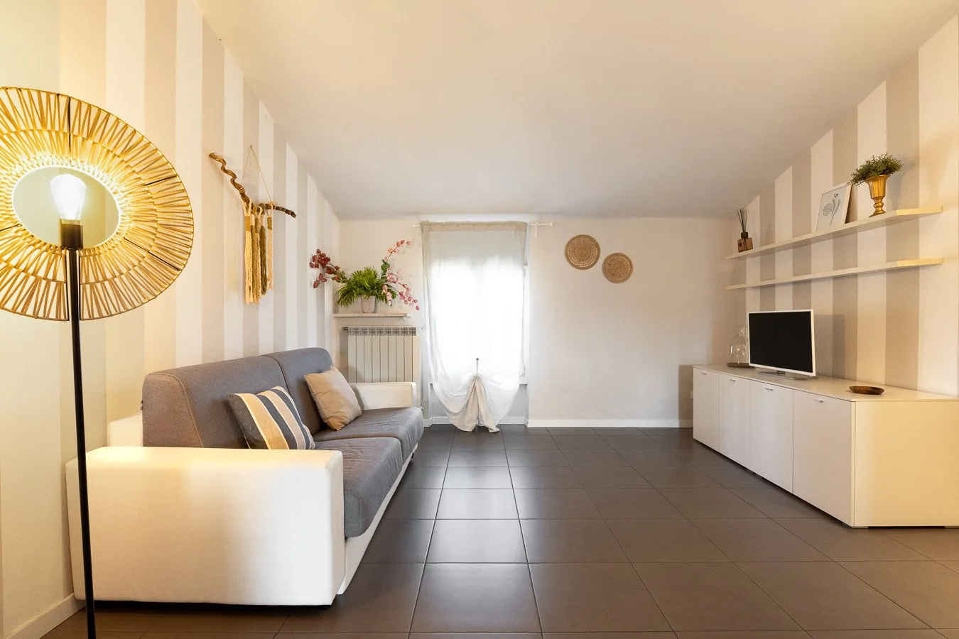 Una sala de estar con asientos, un televisor y una ventana luminosa con cortinas.
