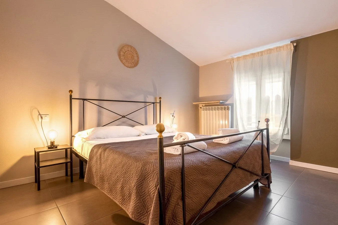 Un dormitorio con una cama de metal y una ventana grande con cortinas.