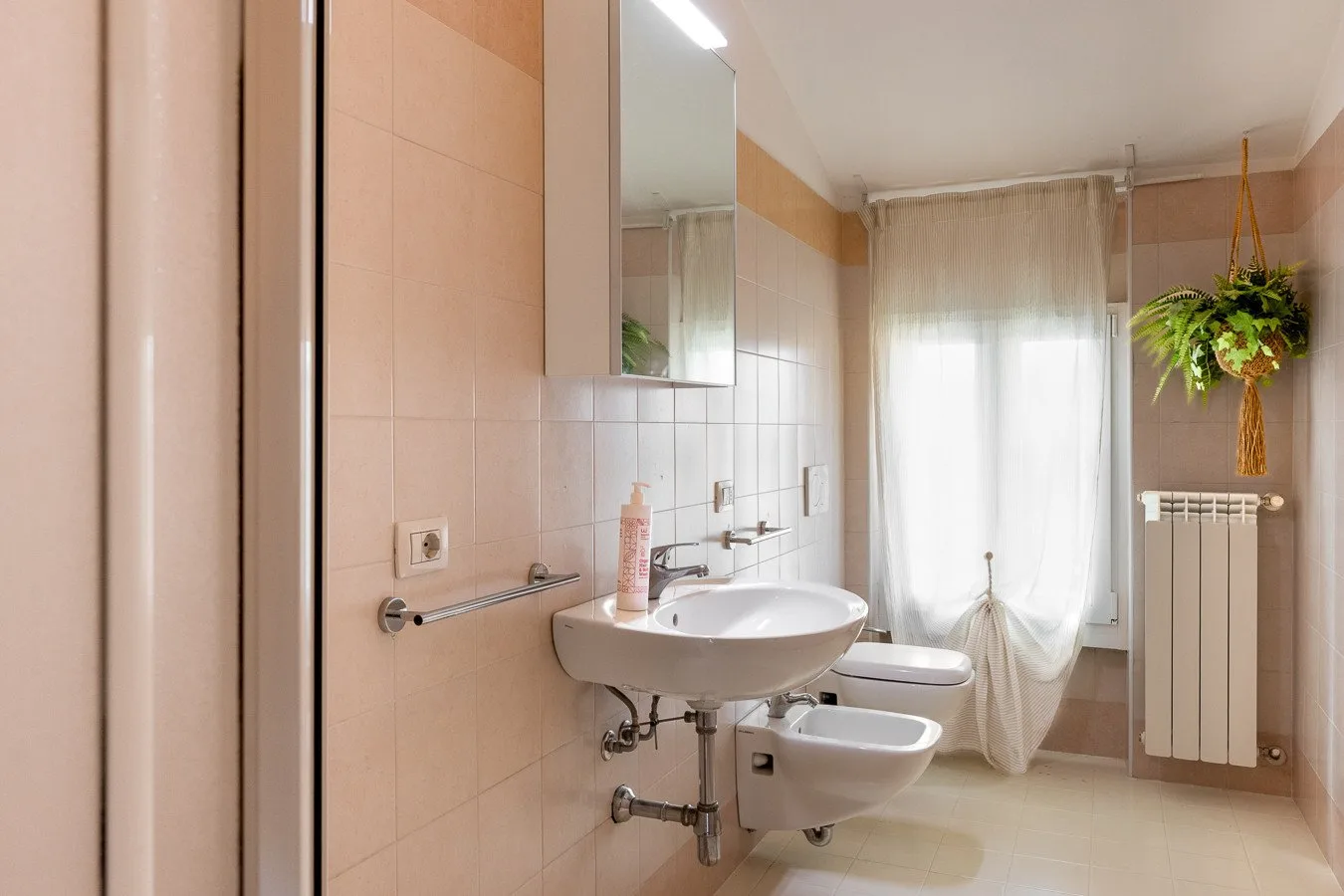Un baño con azulejos, lavabo, inodoro y una ventana con cortina.