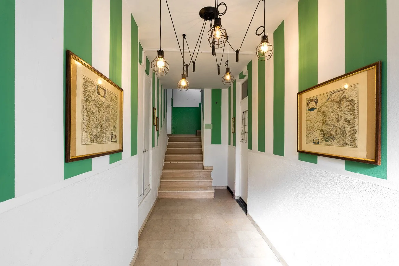 Un pasillo largo con paneles verdes, mapas enmarcados y escaleras al fondo.