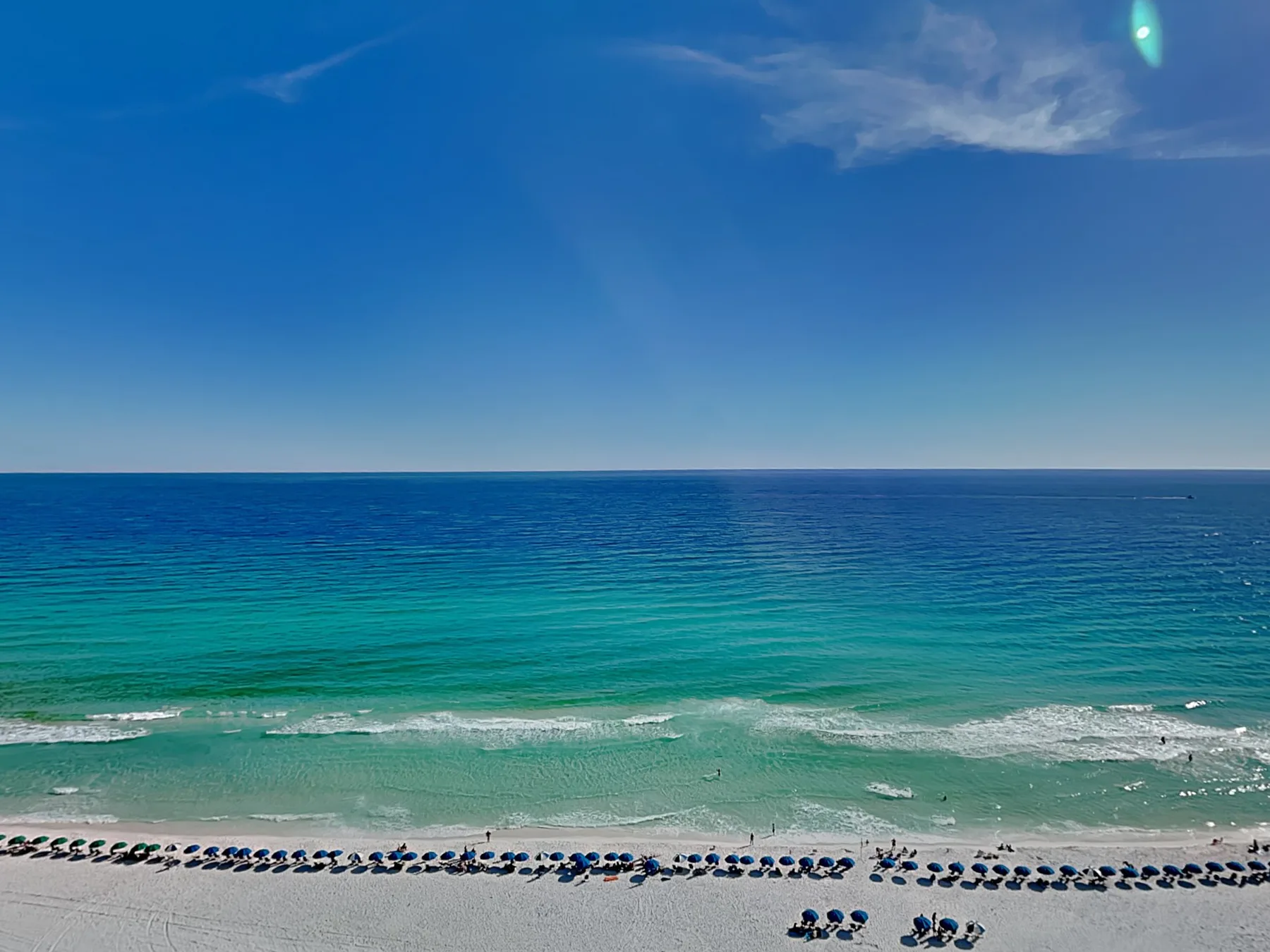 A turquoise sea meets a sandy beach beneath a clear blue sky.