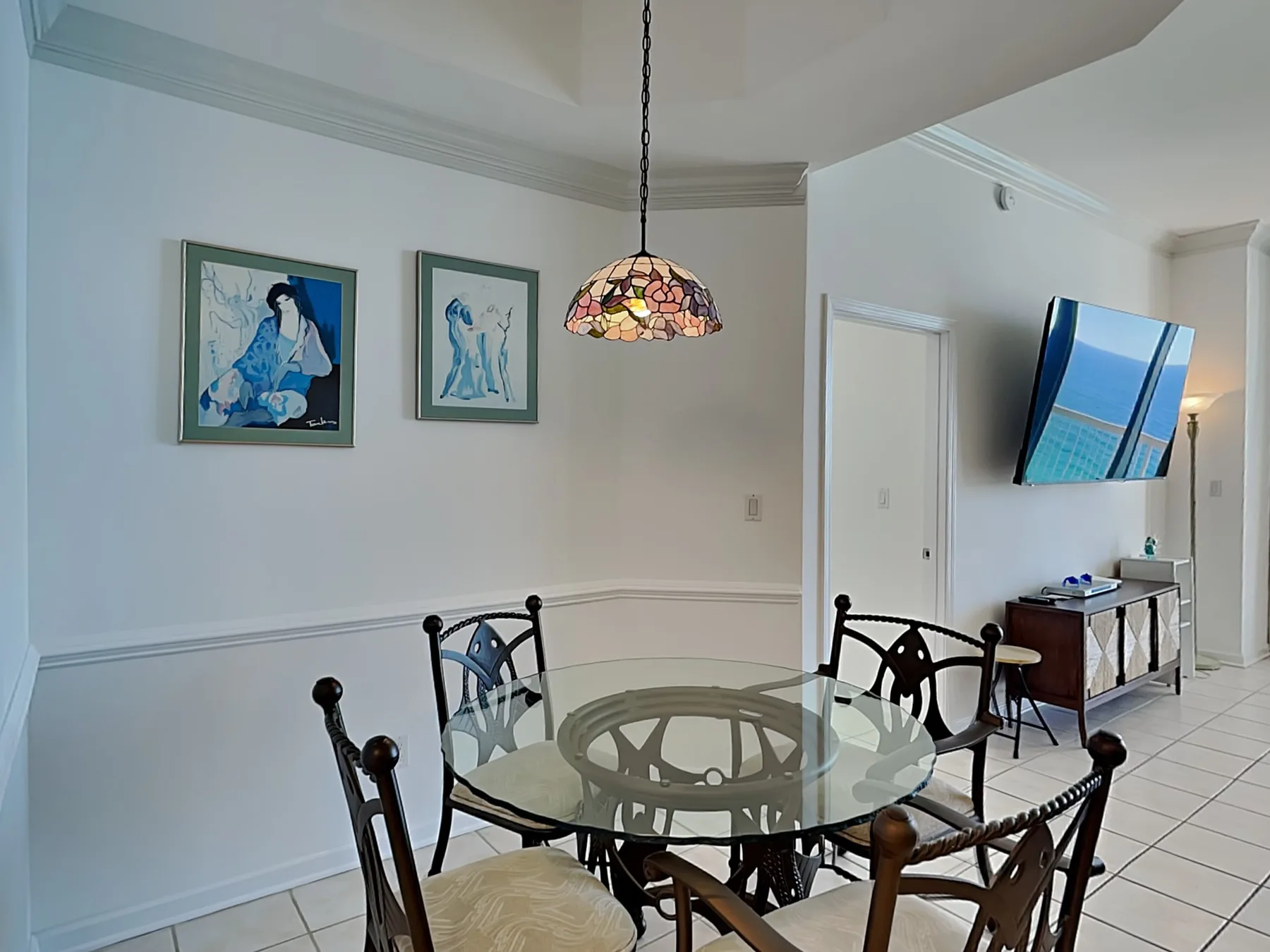 A dining area with a round glass table, chairs, and framed artwork.