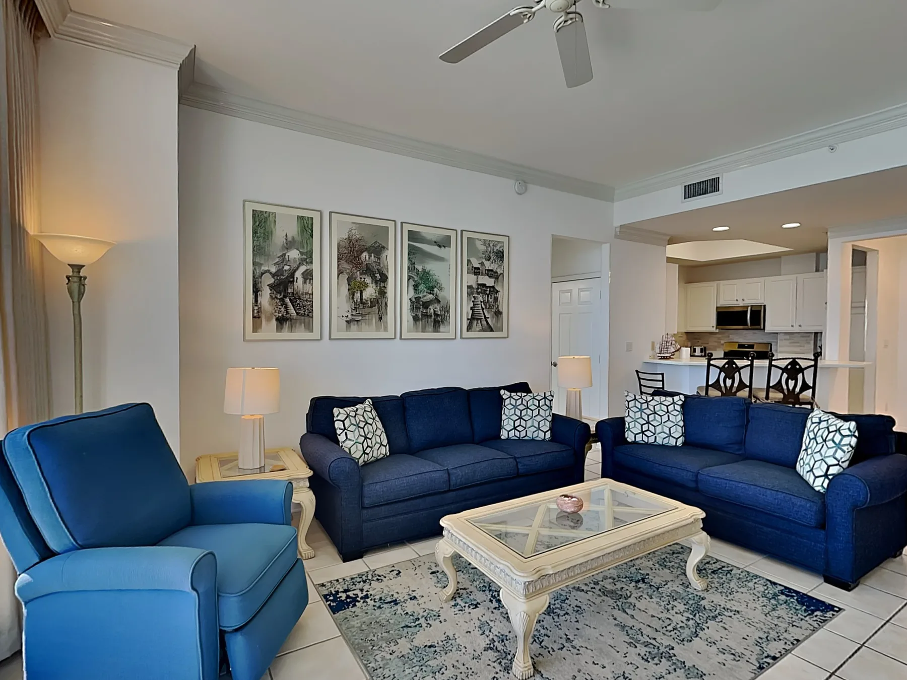 A living room with blue seating, a coffee table, and an open kitchen beyond.