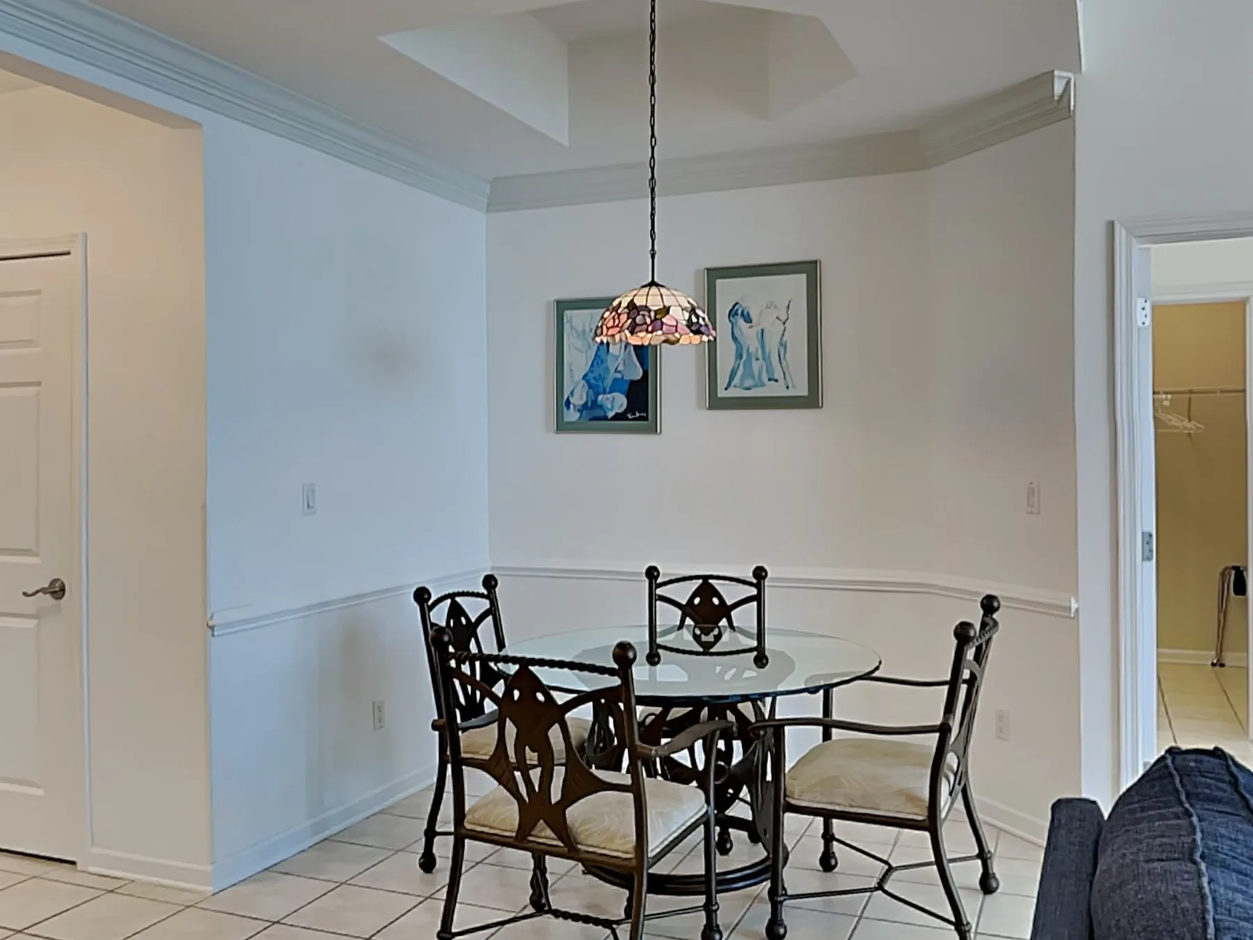 A dining area with a round glass table, metal chairs, and a hanging pendant light.