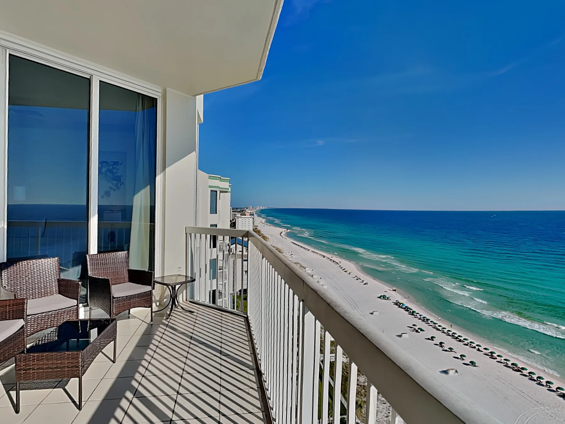 A balcony overlooking the ocean, with seating beside glass doors.