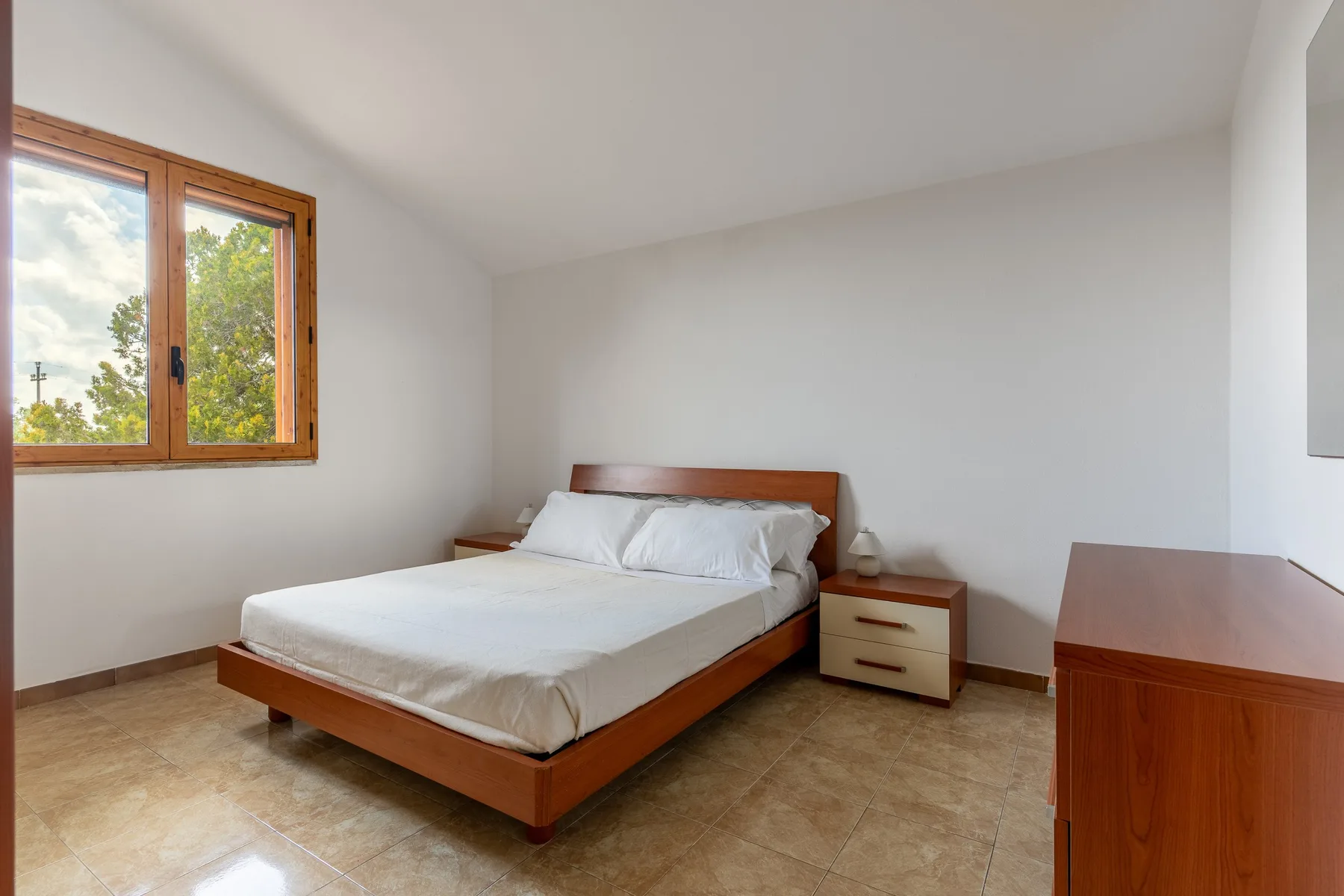 Un dormitorio con una cama de madera, una mesita de noche y una ventana.