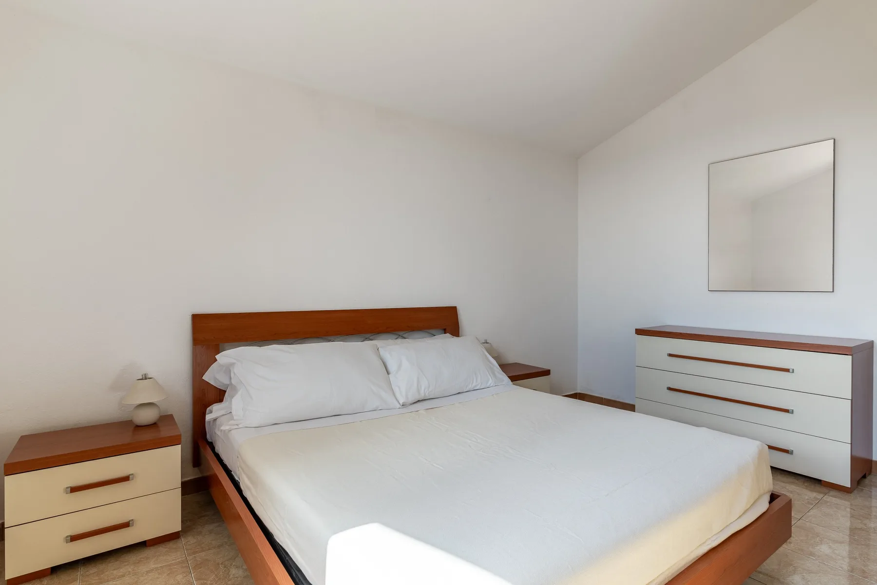 Un dormitorio con una cama bien hecha y una cómoda junto a la pared.