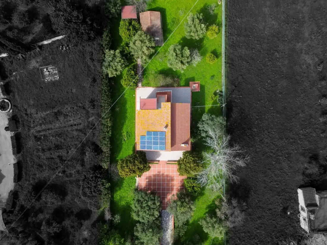 Una vista aérea muestra una casa con patio de baldosas, césped verde y árboles.