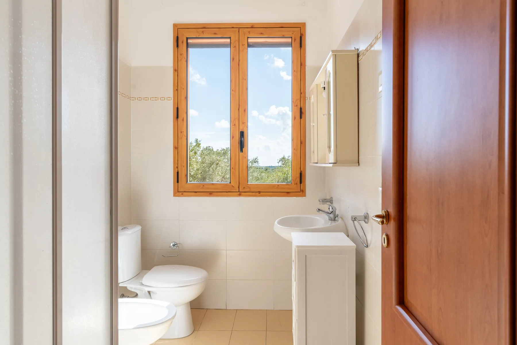 Un baño luminoso con ventana, inodoro, bidé y lavabo.