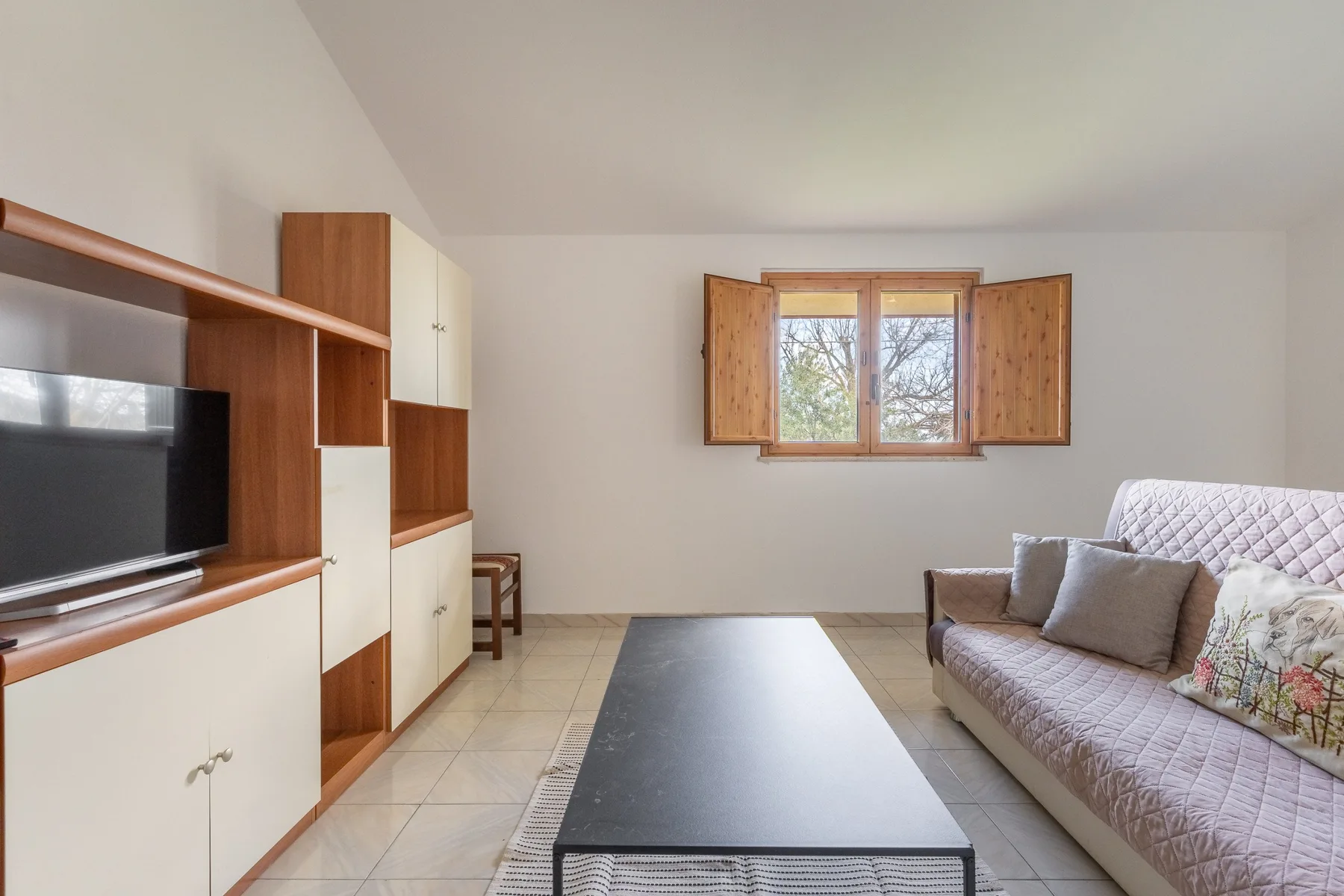 Una sala de estar con mueble de televisión, mesa de centro y asientos junto a una ventana.