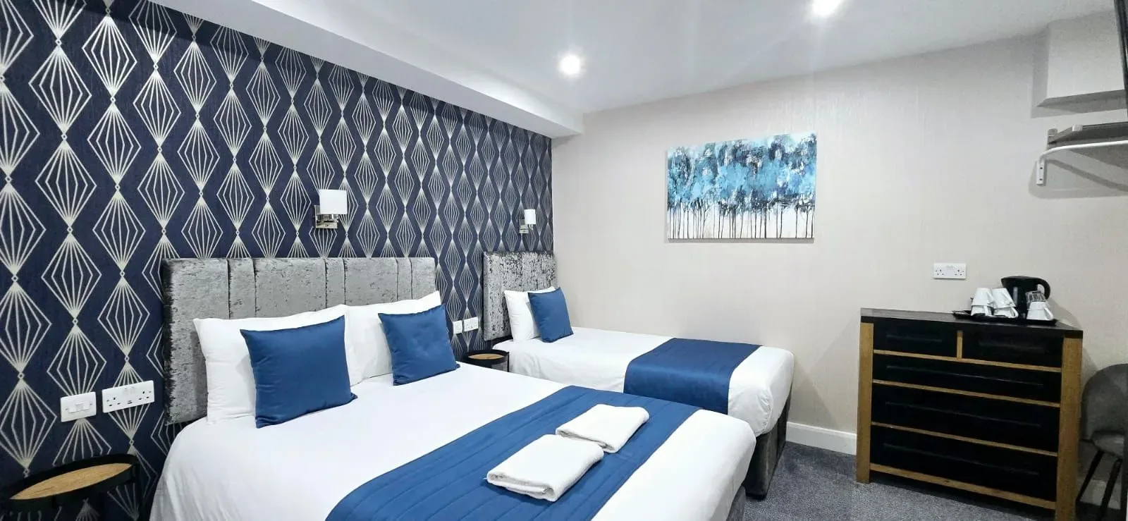 A hotel room with two beds, blue-and-white decor, patterned wallpaper and a dresser.