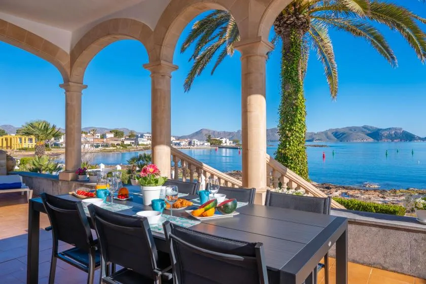 Una terraza exterior con comedor mira al mar, con una mesa bajo arcos de piedra.