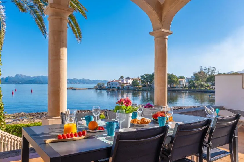Mesa de comedor al aire libre bajo una terraza cubierta, con vistas al agua.