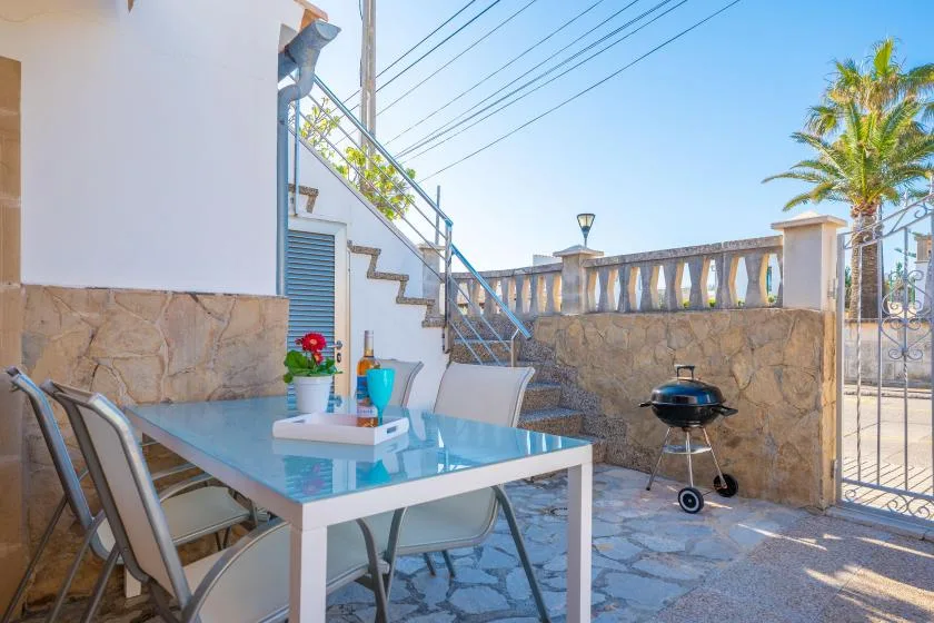 Un patio soleado tiene una mesa de comedor de vidrio, asientos y una parrilla.