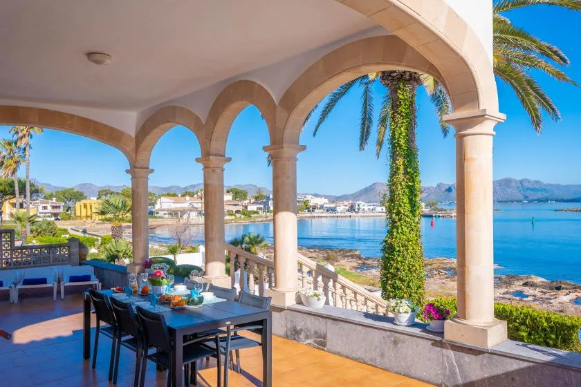 Una zona cubierta para comer al aire libre da a aguas azules a través de arcos.